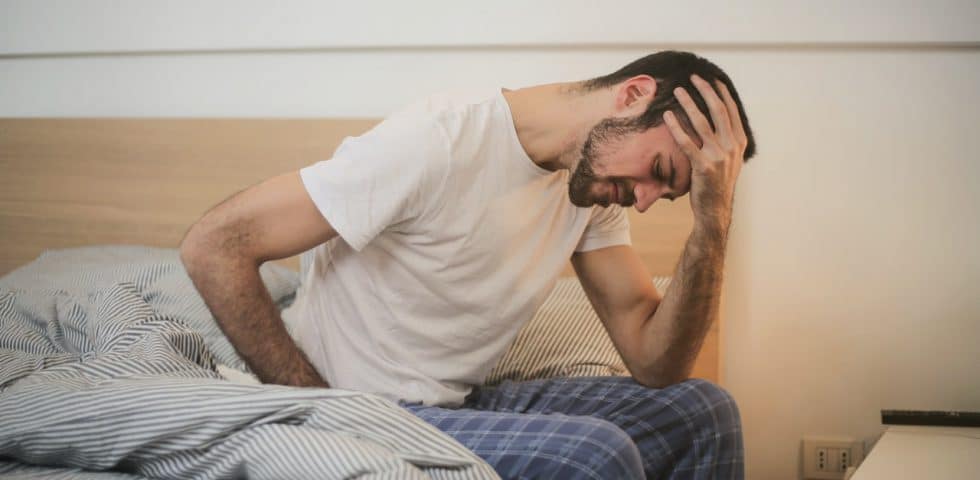 Stressed man getting out of bed with body aches and pains